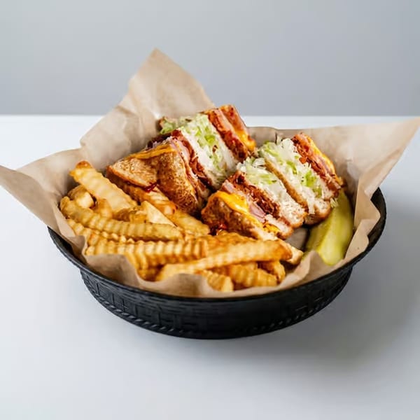 Club sandwich with crinkle-cut fries and a pickle spear in a black basket.