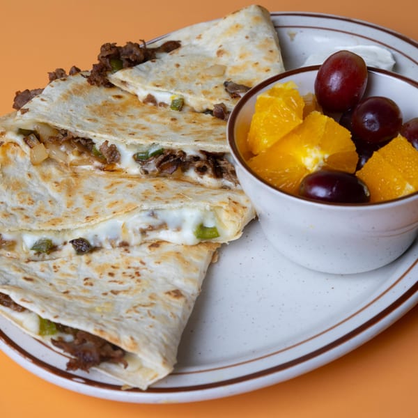 Cheesesteak quesadillas with melted cheese and green peppers, served with a side of fruit.