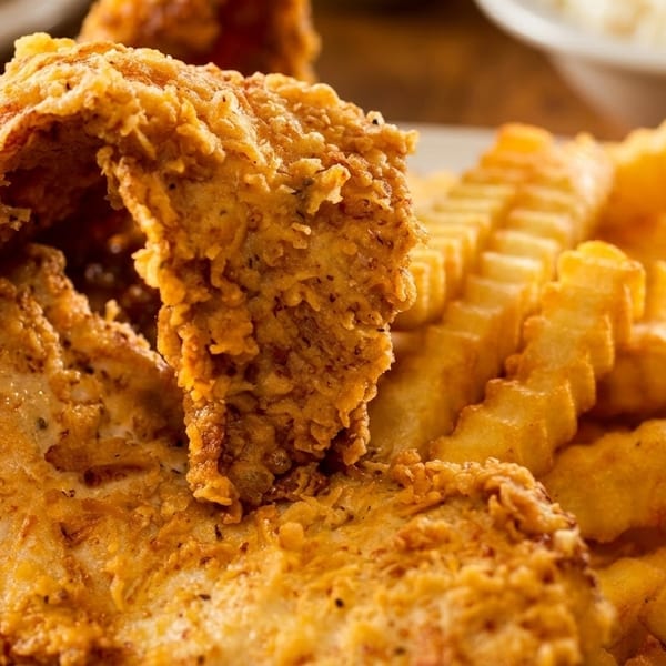 Crispy fried chicken and crinkle-cut french fries on a white plate, with a side dish in the background.