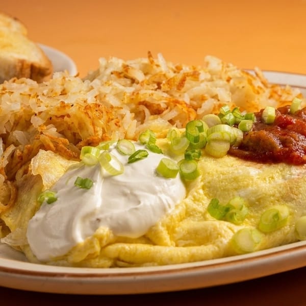 Omelet with hash browns, sour cream, salsa, and green onions, with toast in the background.