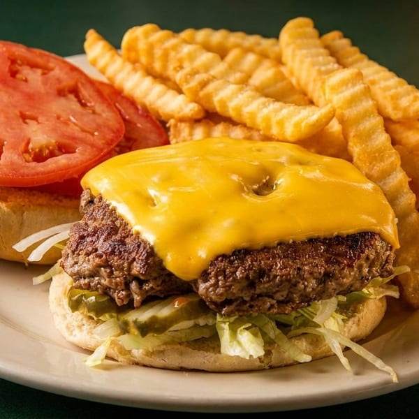 Cheeseburger with melted cheese, lettuce, pickles, and a side of crinkle-cut fries.
